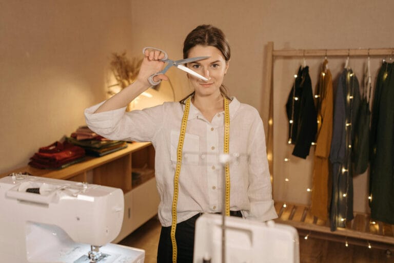 A small business owner standing with a sewing machine, tape measure and scissors