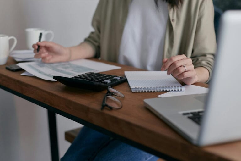 A person working with their laptop and notepad on a small desk
